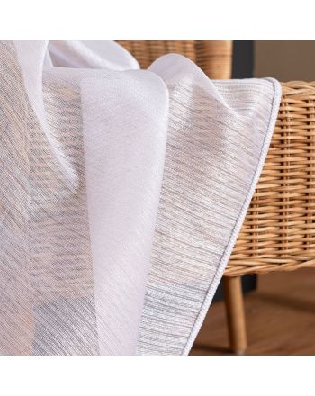 Zbliżenie na strukturę białej firany Sawina z pionowymi, błyszczącymi pasami, udrapowanej na wiklinowym oparciu.